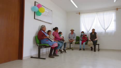 Patients,-including-several-women-wearing-masks-and-children,-are-waiting-outside-of-a-beautiful-clinic-adorned-with-colorful-balloons-in-Ecatepec-de-Morelos,-Mexico