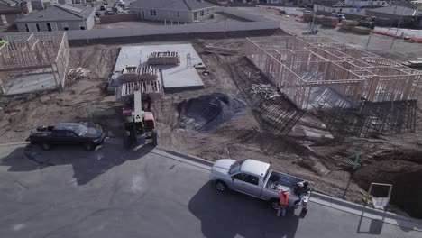 A-drone-observes-an-extendable-forklift-in-action,-gently-lowering-the-third-crate-of-wood-onto-a-cement-foundation-within-a-new-neighborhood-construction-site-where-no-walls-have-been-erected-yet
