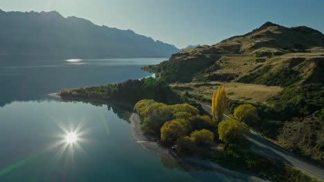 Rural-road-along-shore-of-New-Zealand-lake-with-bright-sunlight-reflection