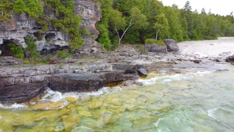 Flying-over-the-clear-waters-of-Lake-Huron-to-the-pristine,-vegetation-covered-shore