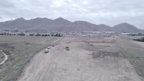 A-drone-shot-from-a-distance-observes-an-elevating-scraper-and-a-water-truck-working-together-to-prepare-land-for-a-future-home-construction-site