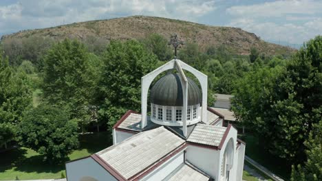 Pedestal-drone-shot-of-St-Petka-Church's-dome,-and-slowly-orbitting-around-the-rest-of-the-buildings-around-the-church,-revealing-the-surrounding-trees-and-mountains