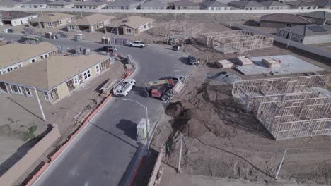A-circling-drone-captures-an-extendable-forklift-in-action,-gently-lowering-a-load-of-wood-on-a-home-construction-site-within-a-new-neighborhood