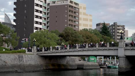 Gente-Cruzando-El-Puente-Motoyasu-En-Hiroshima-Con-Edificios-De-Apartamentos-En-Segundo-Plano.