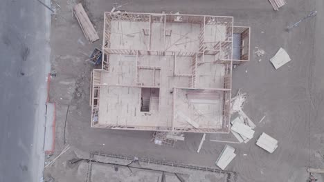 A-drone-gazes-straight-down-onto-various-lots-within-a-construction-site,-revealing-each-stage-from-bare-dirt-with-no-foundation-to-a-partially-built-house-with-a-laid-out-roof