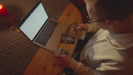 Man-look-at-old-family-photos-near-laptop-and-red-candle-on-wooden-table