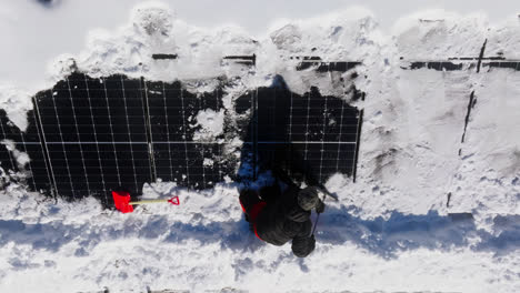 Aerial-view-above-a-house-owner-cleaning-his-snowy-solar-panels-on-a-winter-day