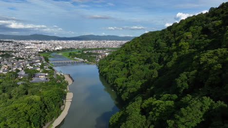 Flying-close-to-forest,-toward-the-skyline-of-Kyoto,-summer-in-Japan---Aerial-view