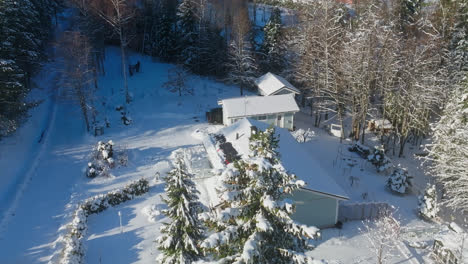 Aerial-view-around-a-house-owner-on-the-roof,-cleaning-snowy-solar-cells,-winter-day