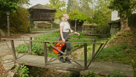 Young-woman-guitarist-crosses-wooden-footbridge-Bulgarian-village