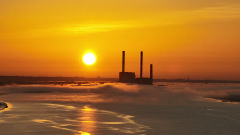A-long-focal-range-drone-shot,-in-lateral-motion-or-side-tracking,-of-a-french-coal-power-plant-factory-shut-down-,-near-the-Loire-river,-with-mist-and-haze-and-fog,-at-sunrise