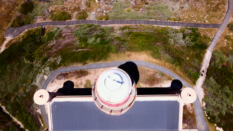 Top-down-aerial-tilt-up-view-reveals-Cape-Agulhas-lighthouse-on-rugged-coastline