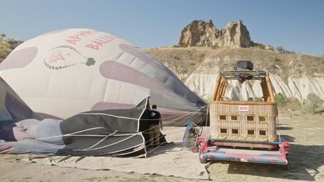 Man-inflating-tourist-hot-air-balloon-envelope-sunny-day-mountain-area