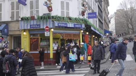 Pizzeria-on-the-corner-of-Paris,-many-pedestrians-walking-down-the-street-in-the-middle-of-winter