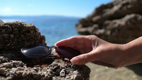 Frau-Setzt-Sonnenbrille-Auf-Felsen-Und-Geht-Am-Strand-Schwimmen,-Urlaubssommerstimmung