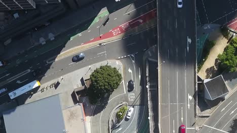 Drone-top-down-pan-across-turning-intersection-lane-in-city-half-covered-by-shadow