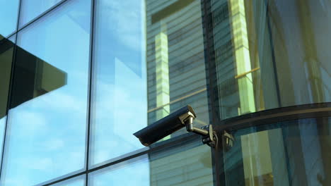 Überwachungskamera-An-Der-Reflektierenden-Glasfassade-Eines-Modernen-Gebäudes-Mit-Verzerrter-Reflexion-Der-Stadt