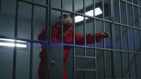 Close-Up-of-Prisoner-in-Orange-Uniform-Holding-Metal-Bars-in-Prison-Cell----------(Stock-Footage)