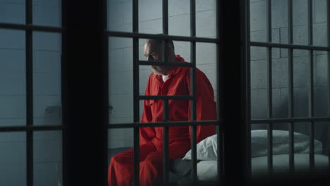 Criminal-Sits-on-the-Bed-in-Prison-Cell-Looks-at-Barred-Window----------(Stock-Footage)