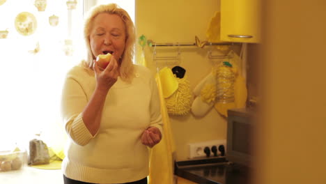 Mujer-Mayor-Comiendo-Manzana-En-La-Cocina-Amarilla