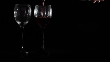 Red-wine-is-poured-into-two-glasses-on-black-background