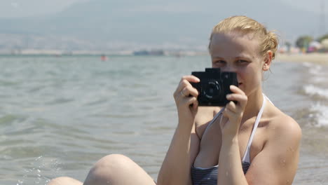 Smiling-woman-taking-a-photo-at-the-seaside-with-her-vintage-camera