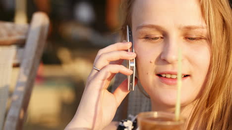 Young-woman-talking-on-mobile-and-drinking-coffee-cocktail