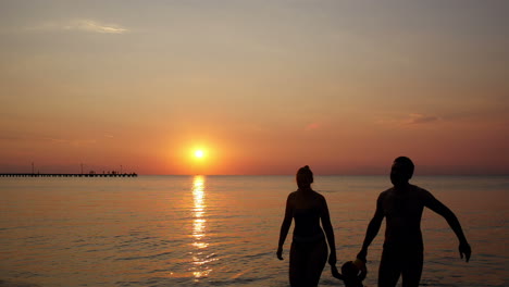 Junge-Familie-Am-Strand-Unter-Einem-Farbenfrohen-Sonnenuntergang