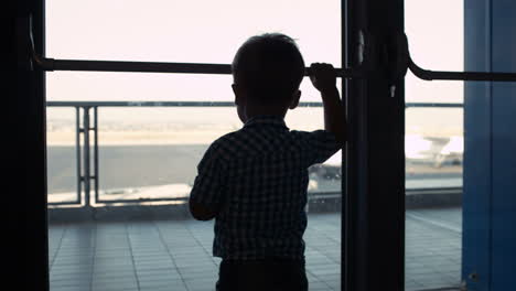 Kleiner-Junge,-Der-Durch-Das-Fenster-Im-Flughafen-Schaut