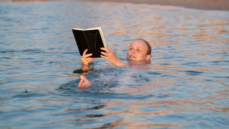 Woman-smiling-as-she-reads-a-book-while-swimming