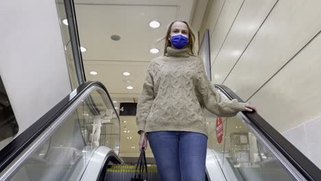 Woman-in-medical-mask-getting-downstairs-by-escalator-in-trade-centre