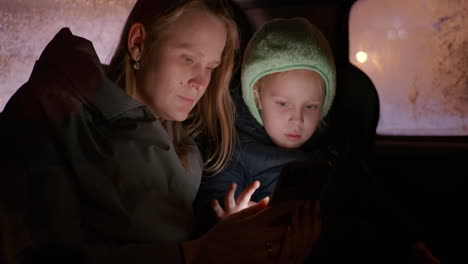 Madre-E-Hijo-Usando-El-Teléfono-Durante-Un-Viaje-Nocturno-En-Automóvil