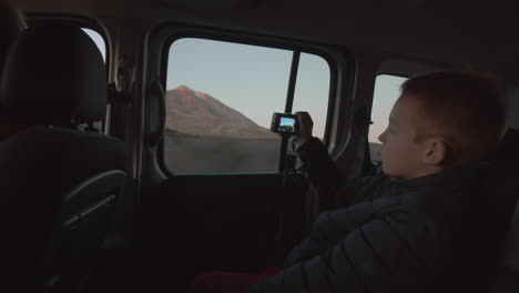 A-boy-on-the-backseat-of-the-driving-car-shooting-the-mountain-landscape