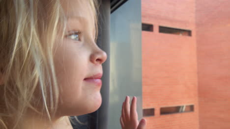 Cheerful-and-curious-little-girl-looking-outside-through-the-window