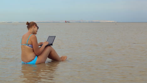 Woman-using-laptop-sitting-in-the-sea