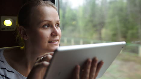 Young-woman-using-touch-pad-sitting-by-the-window-in-train