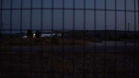 Car-passing-by-night-view-from-behind-the-wire-metal-fence