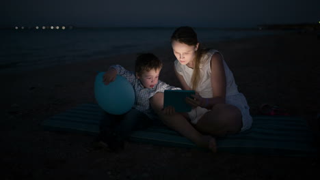 Mother-and-son-with-pad-by-the-sea-at-night