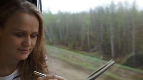 Young-woman-making-notes-while-traveling-by-train