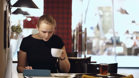 Young-woman-sitting-in-cafe-with-pad-and-drinking-coffee