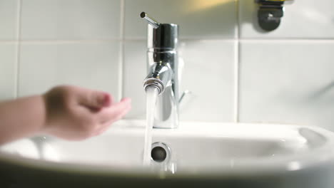 Childs-hand-touching-water-pouring-from-tap