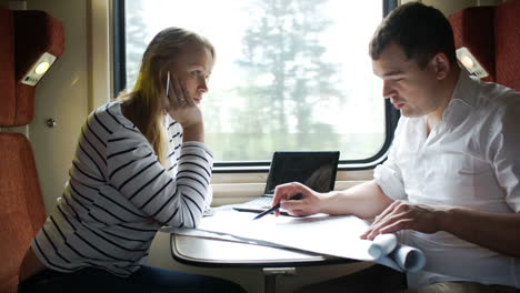 Man-and-woman-discussing-drawing-during-business-trip-in-the-train