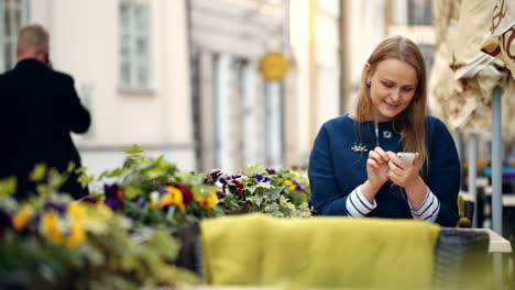 Woman-using-her-smartphone-sitting-in-outdoor-cafe