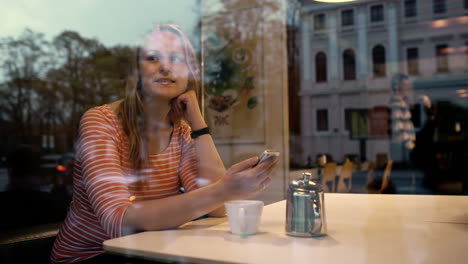 Woman-with-phone-in-cafe-enjoying-outside-view