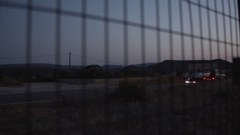 Looking-at-country-road-in-the-dusk-through-wire-metal-fence
