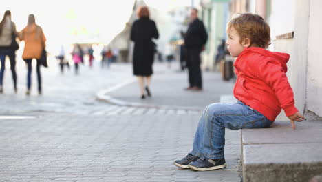 Little-boy-sitting-alone-in-the-street-people-passing-by