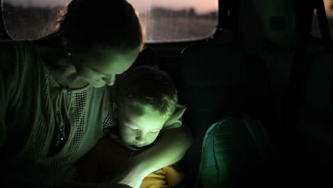 Mother-and-son-using-touch-pad-in-car-at-night