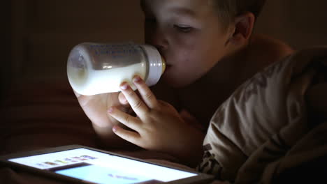 Junge-Trinkt-Milch-Aus-Der-Flasche-Und-Schaut-Auf-Das-Touchpad