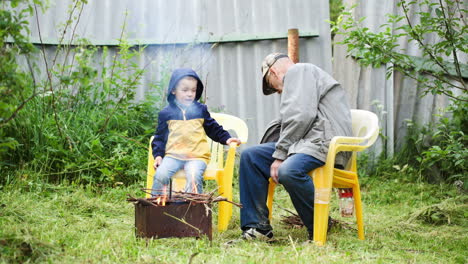Grandfather-and-his-grandson-sitting-by-the-fire-outdoor