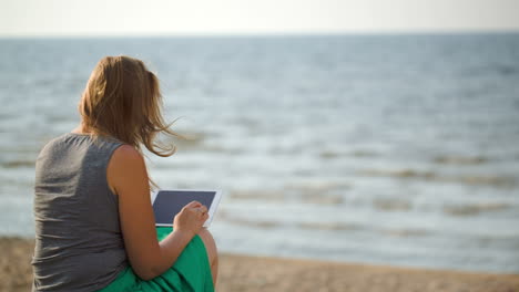 Woman-sitting-on-beach-by-the-sea-with-touch-pad